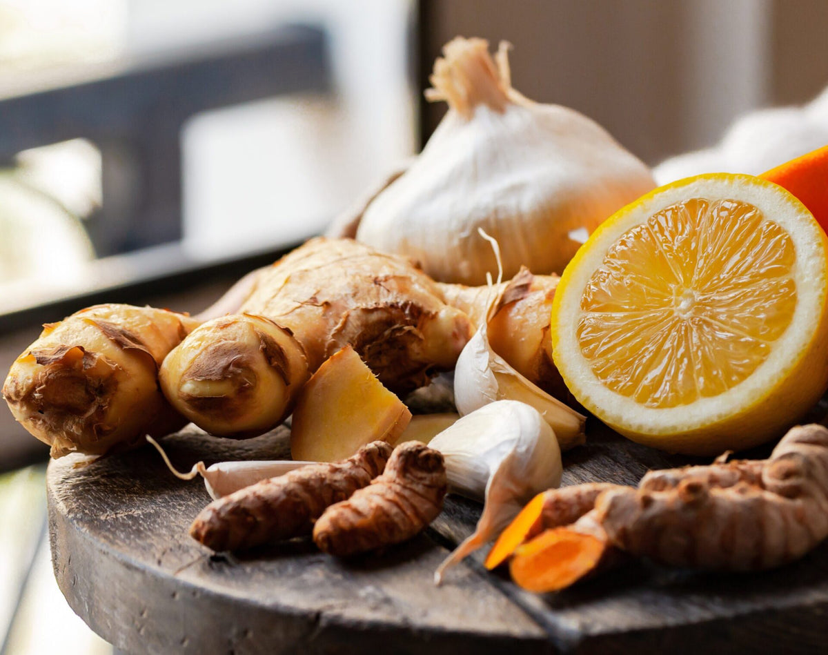 Knoblauch, Ingwer, halbierte Zitrone und Kurkuma als Zaubertrank-Zutaten auf einem runden Holzbrett