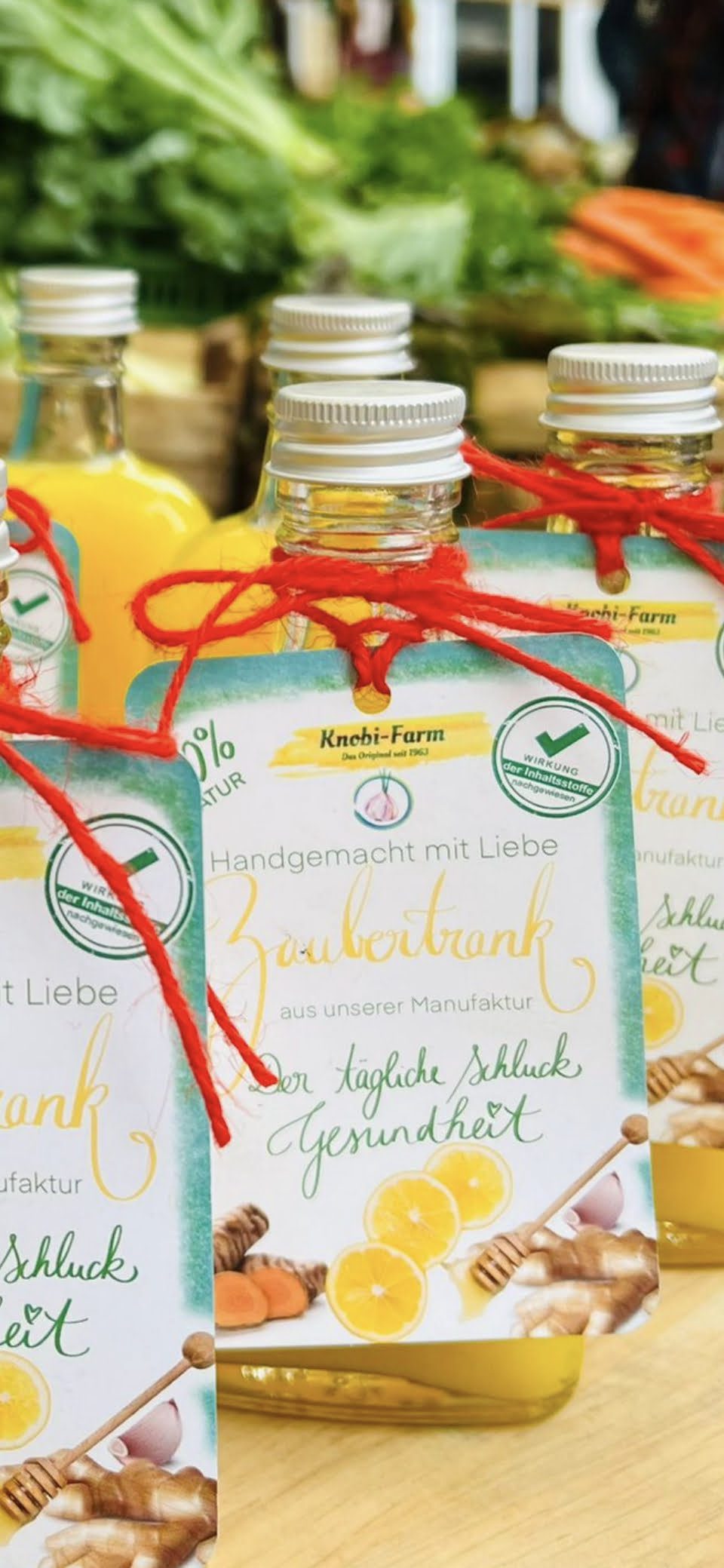 Mehrere Flaschen Zaubertrank mit Anhängern und roter Kordel, dahinter frisches Gemüse am Marktstand