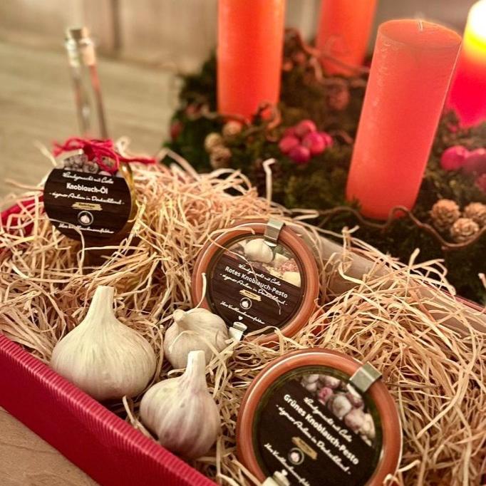 Geschenkkorb mit Knoblauch-Öl, rotem und grünem Knoblauch-Pesto und frischen Knollen, dahinter Adventskerzen