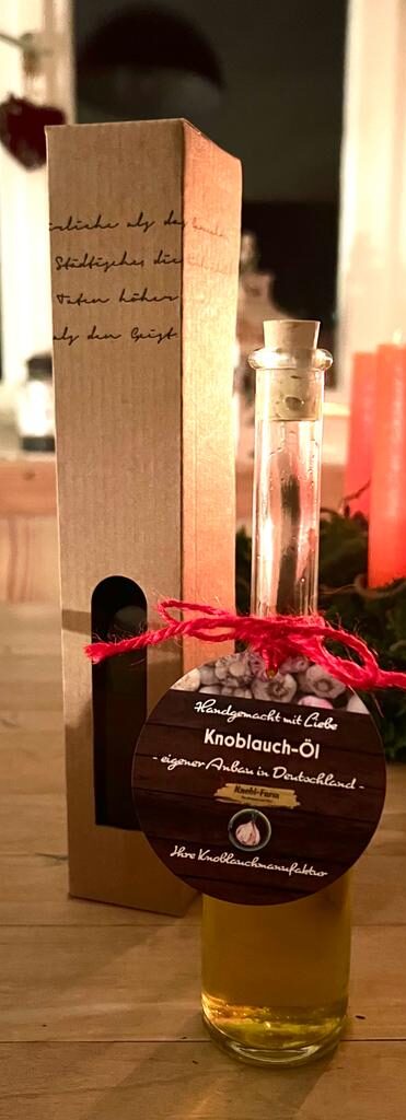 Schmale Flasche Knoblauch-Öl mit Etikett und roter Kordel neben einer Geschenkverpackung aus Karton