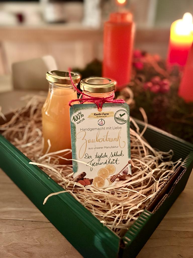 Zwei Flaschen Zaubertrank mit Anhänger in einer grünen Geschenkbox mit Holzwolle vor Kerzenlicht