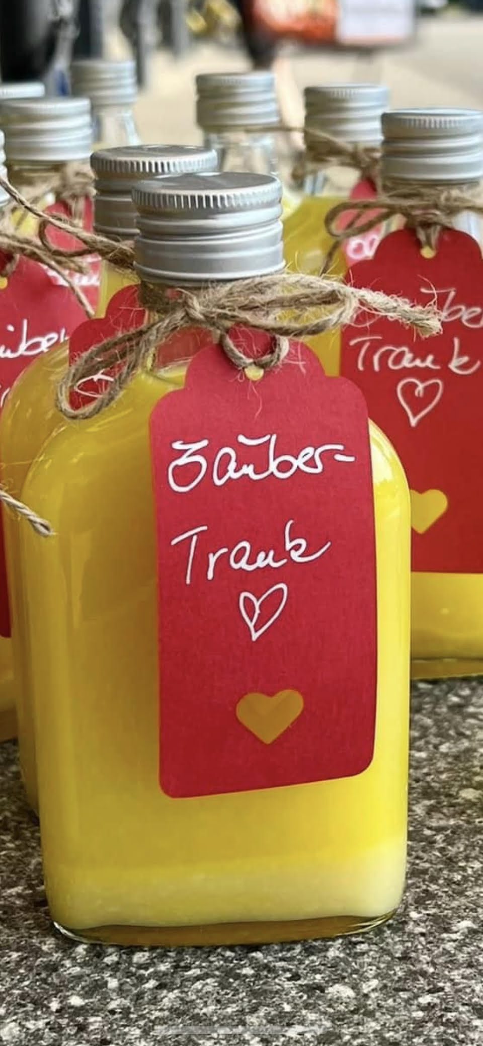 Mehrere Flaschen Zaubertrank mit gelbem Inhalt und roten handbeschrifteten Anhängern